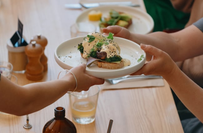 A plate of eggs on toast being handed to a customer.