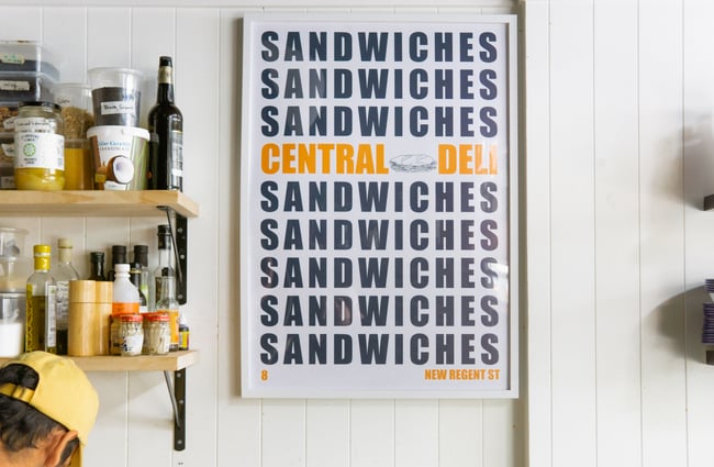 A large Central Deli Sandwiches poster framed on a wall.