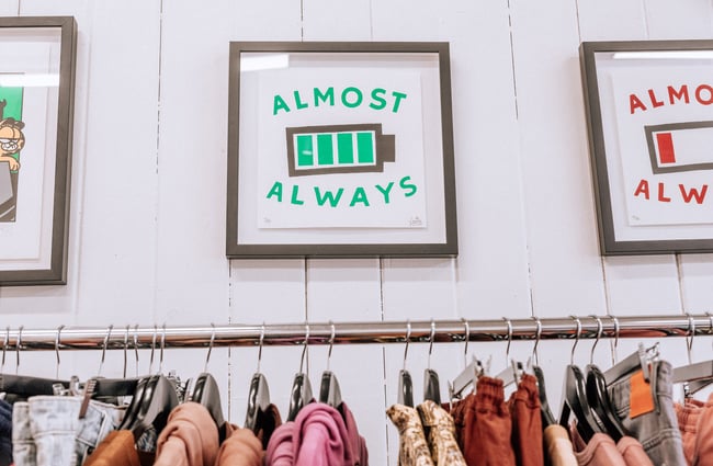 Three framed art works on the wall above a rack of clothing.