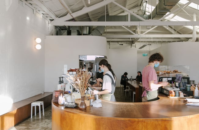 Two employees behind behind the wooden counter taking orders and making coffees.