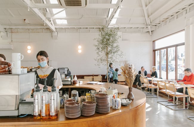 Customers sitting around tables inside a brightly lit Child Sister Cafe.
