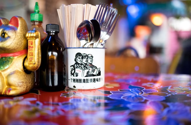Cutlery in white mugs on a colourful table.