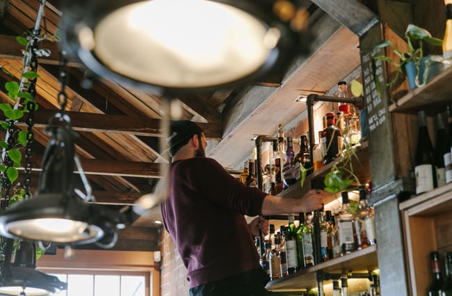 A staff member looking for a bottle of liquor high up on a shelf.