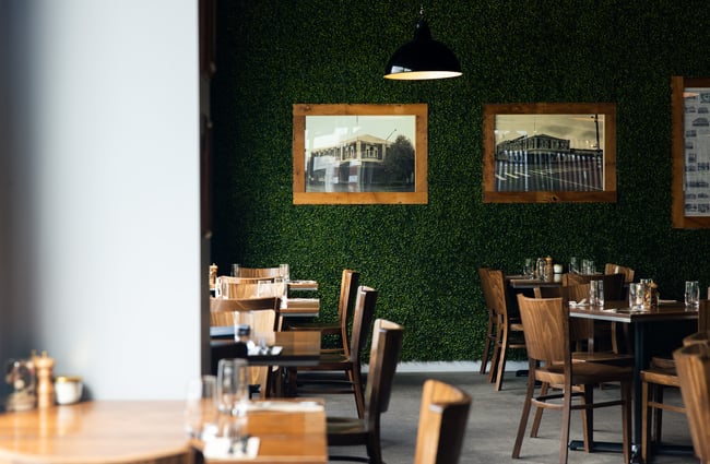 Tables and chairs inside a wooden and green decorated restaurant.