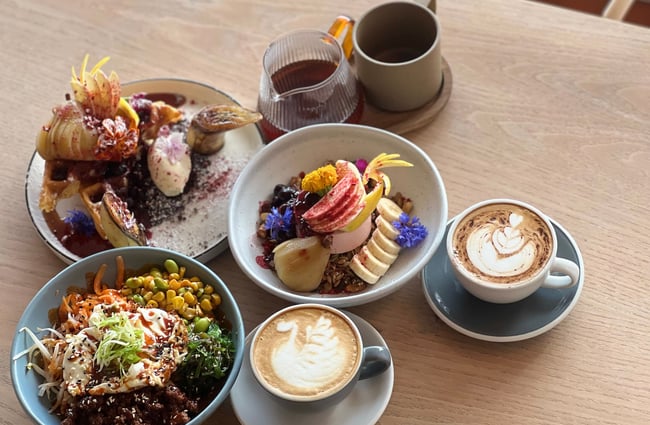 Three dishes, two milky barista coffees and a little jug of filter coffee on a table at Comes & Goes in Petone.