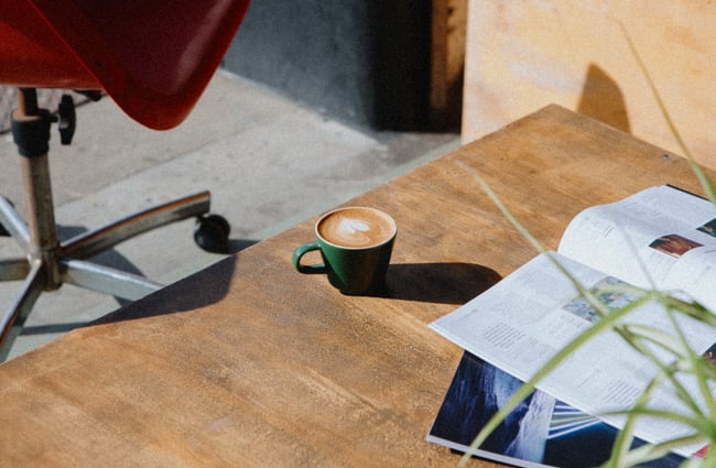 A white coffee in a dark green mug sitting on a wooden table in the sunshine.