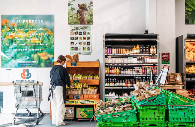 Person standing in front of banana stand next to drink fridge