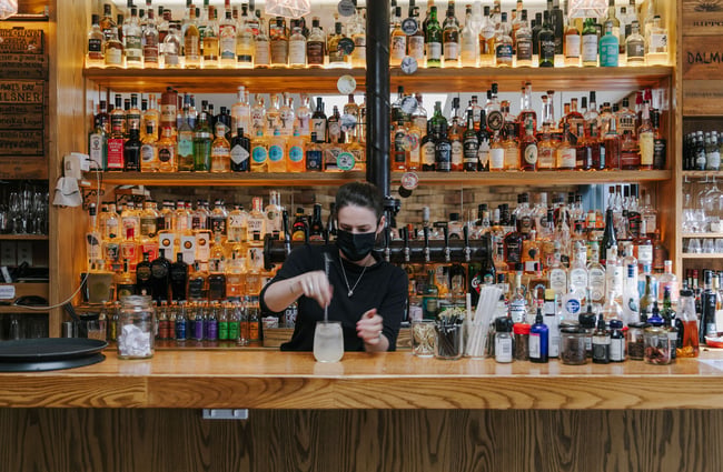 Woman stirring a cocktail with lots of bottles on shelves behind her at Cork, Wānaka.