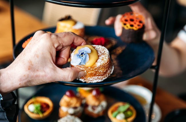 Diner selects a small cake from the tiered tray at Country Road High Tea.