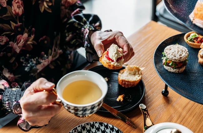 Diner holding a cup of tea in one hand and a scone in the other hand at Country Road High Tea.
