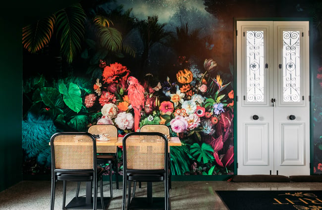 Floral wallpaper is on the walls behind table and chairs at Country Road High Tea.
