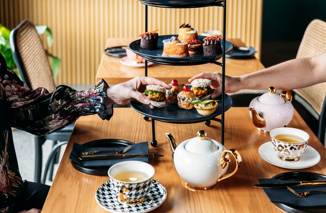 Tiered tray of savoury and sweet food items, with diners reaching to select items at Country Road High Tea.