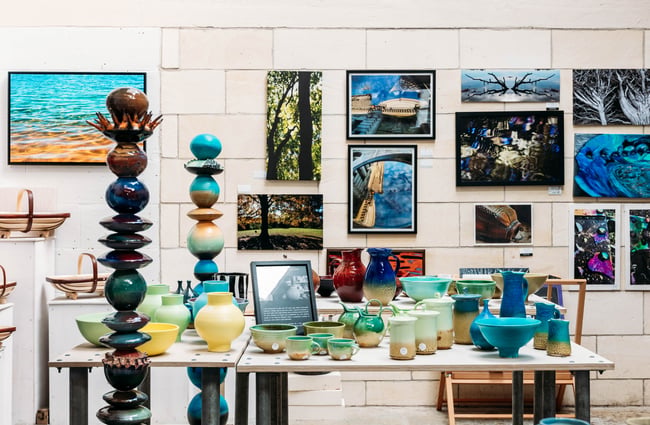 Unique sculptures and ceramics on table in front of a wall filled with artistic photography at Crafted Gallery in Ōamaru