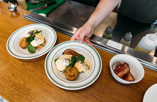 An outstretched arm places a plate of bacon and eggs and hollandaise on the pass at Cream Eatery in Hamilton.
