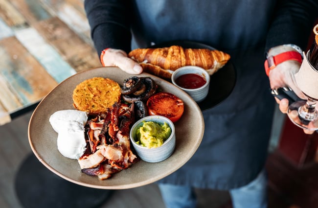 Hands holding plates of a cooked breakfast.