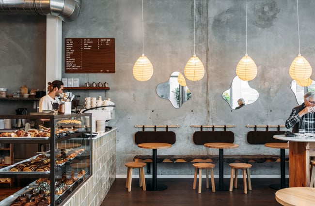 Barista behind food cabinet and seating area at Crumb.