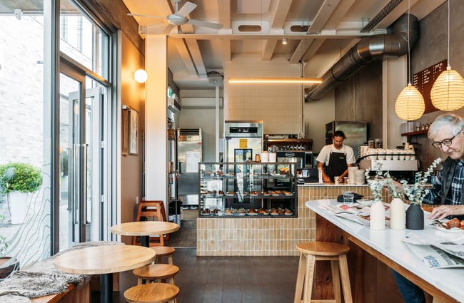 Tables and chairs in the cafe space with the food cabinet and barista in the background at Crumb.