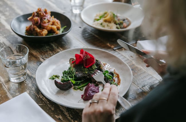 Looking over the shoulder of a person eating a meal with a knife and fork.