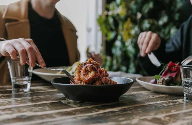 A lady putting a fork into a black bowl with a pile of fried food.