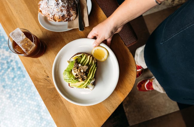 A photo looking down on avocado on toast with a slice of lemon.