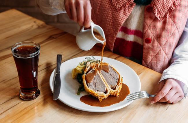 A close up of gravy being poured on a beef wellington.