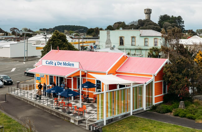 Cafe building at De Molen showing the outdoor seating area with tables and umbrellas.