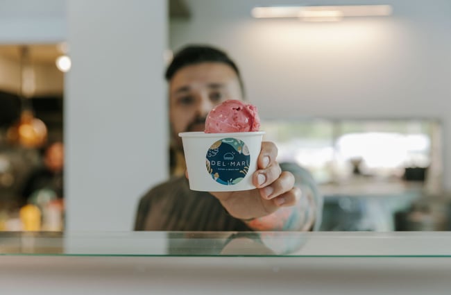 A man handing a tub of gelato over to a customer.