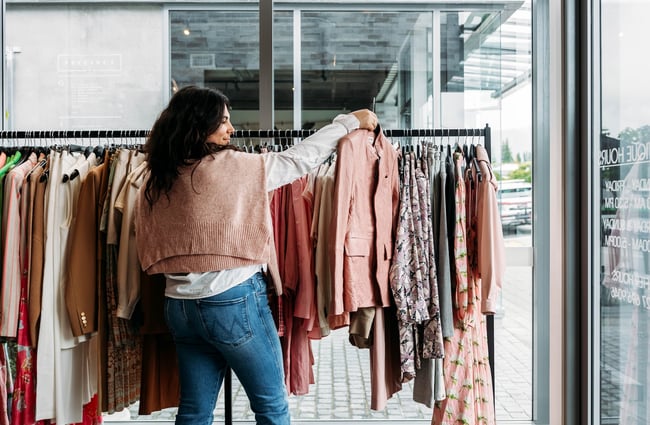 A woman pulling out a pink blazer from a rack of pink and brown garments against the window in DEVàl Boutique, Wānaka.