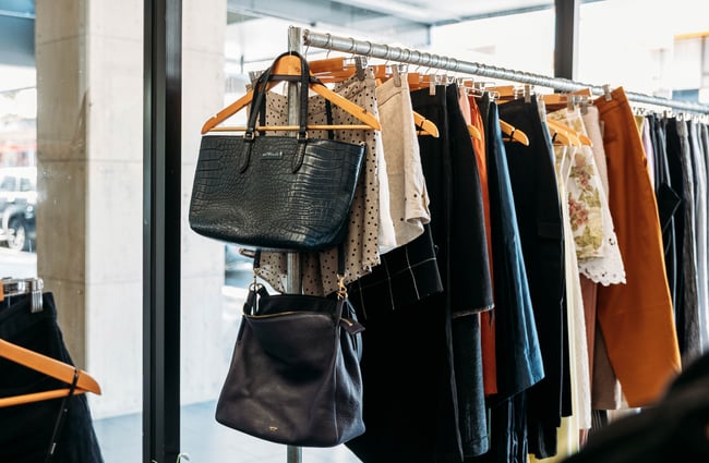 Handbags are hung at the front of a clothing rack at Different Avenue.