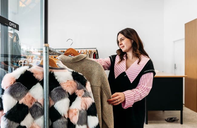 Shop manager holds an item of clothing at the rack at Different Avenue.