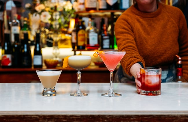 Cocktails lined up on a row on a bar.