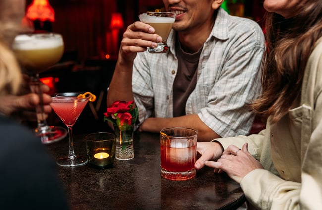 Hands holding cocktails around a table.
