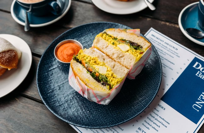 Thick egg sandwich cut in half on a plate with a spicy orange sauce next to it