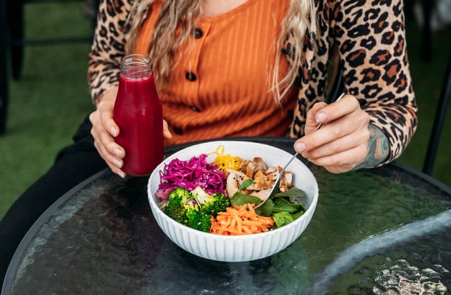 A customer sits at a table with a salad bowl and juice in front of them at Dripping Bowl.