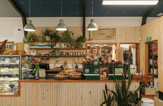 A female barista behind the coffee machine stacks cups.