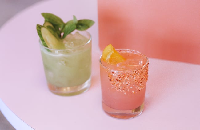 One green and one pink cocktail sitting on a table.