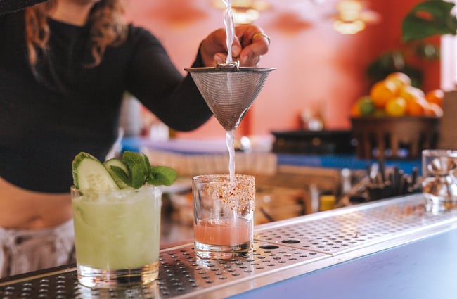 A bar staff making two cocktails in short glasses on the bar.