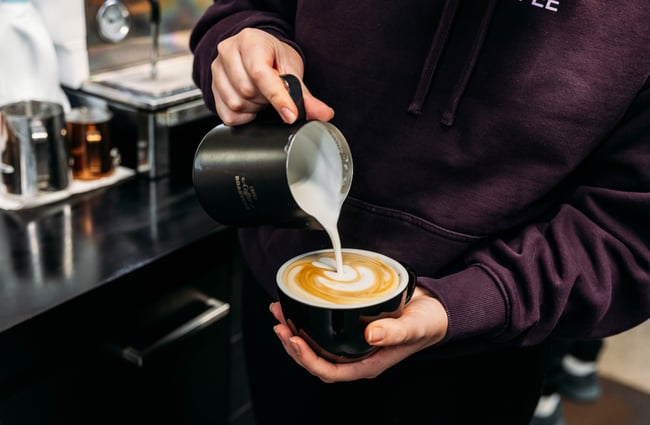 Barista pouring milk into a cup of coffee at Ebony Coffee Roasters