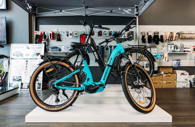 An electric blue e-bike displayed on a low white plinth inside Electrify.