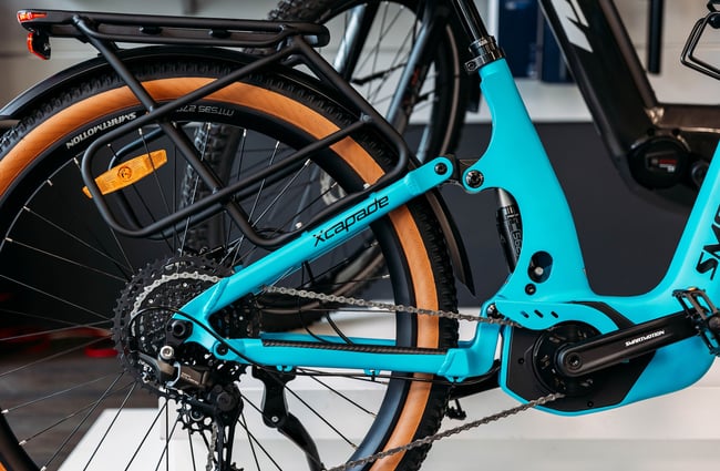 Close up of the rear triangle and drive train of a blue bike with 'xcapade' printed along one of the tubes.