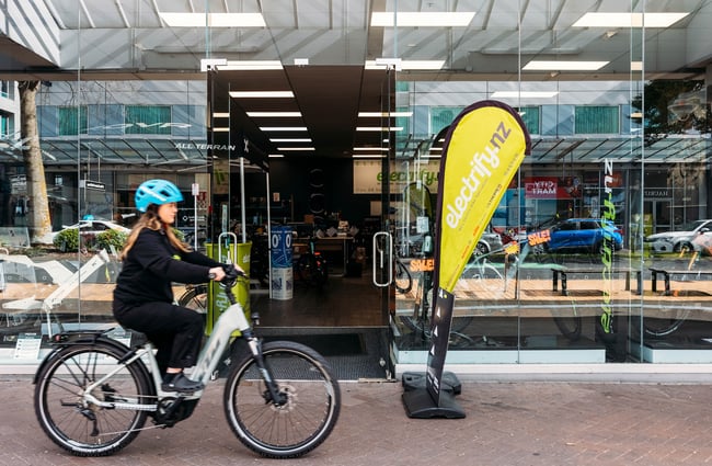 The glass frontage of Electrify bike store with a person cycling along in front of it.