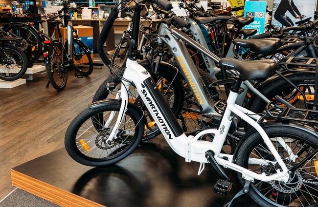 A white electric bike at the front of a row of bikes on a low plinth inside the store.