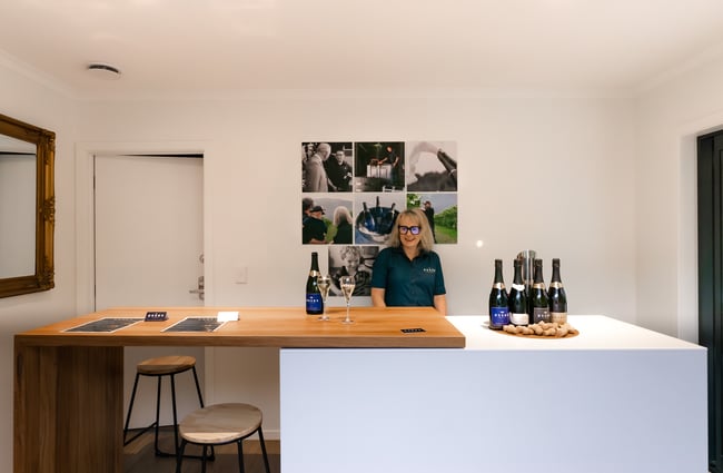 A blonde woman wearing black glasses smiling behind a counter.