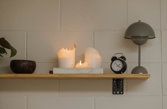 Close up of three white candles burning on shelf next to lamp and cute analogue alarm clock