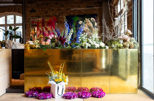A gold planter filled with vibrant flowers at entrance of luxurious retail shop in Auckland