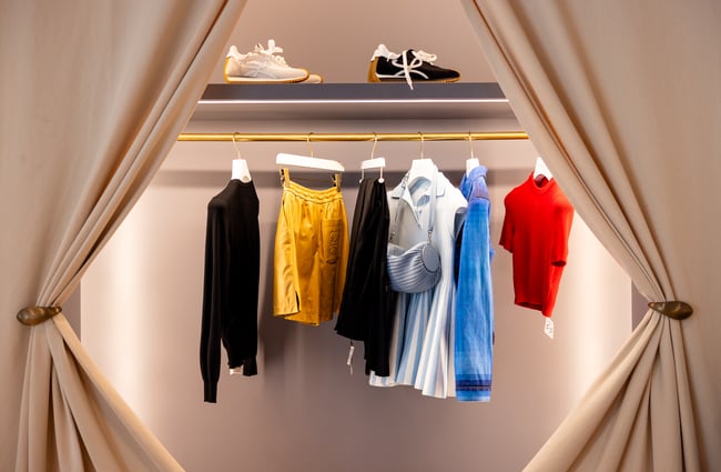 Clothes hanging on a rack framed by draped cream curtains
