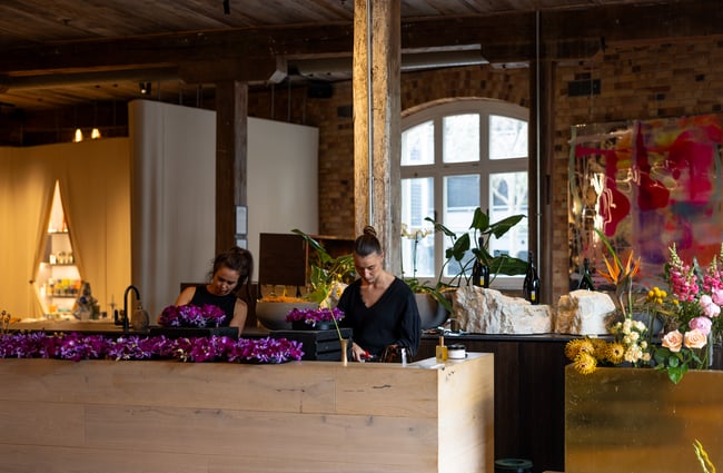 Two florists putting together bouquets behind wooden counter at luxury retail shop