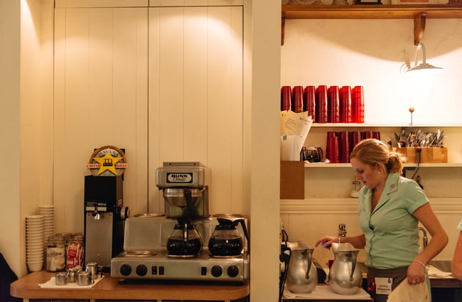 Waitress pouring water by coffee machine.