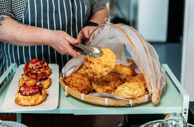 Waiter picking up a cheese scone from under mesh cloche with tongs