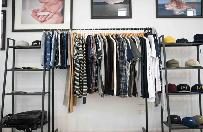 A clothing rack full of clothes in front of artwork on the wall.